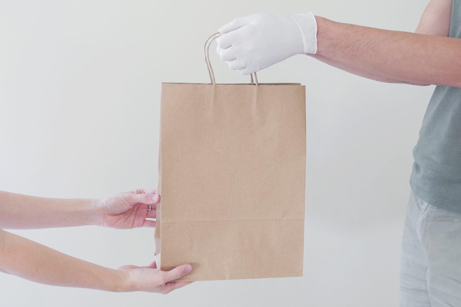 Hand with gloves giving eco paper bag, take away food, home delivery, donation concept