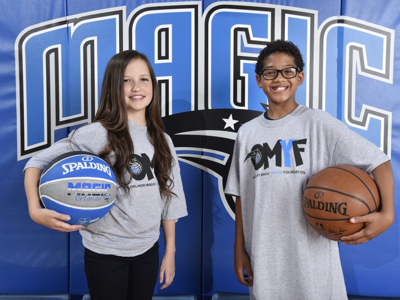Two children holding basketballs in front of Orlando Magic banner